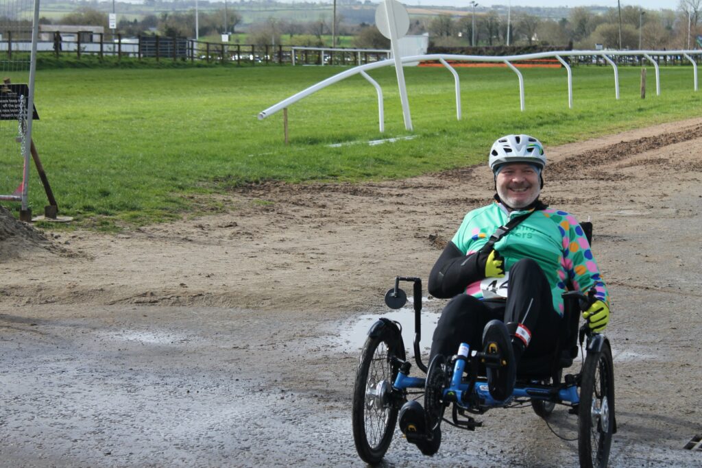 Man riding a recumbent trike on a racecourse during the day.