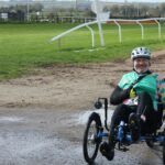 Man riding a recumbent trike on a racecourse during the day.